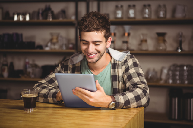 Smiling hipster having coffee and using tablet computer at coffee shop
